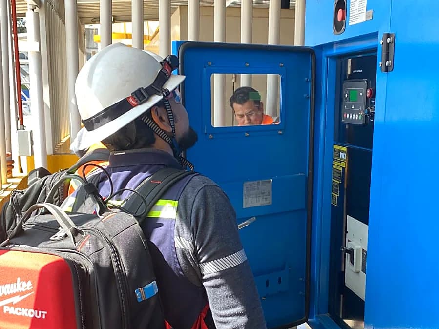 Técnico con casco y arnés frente al tablero de un equipo de enfriamiento
