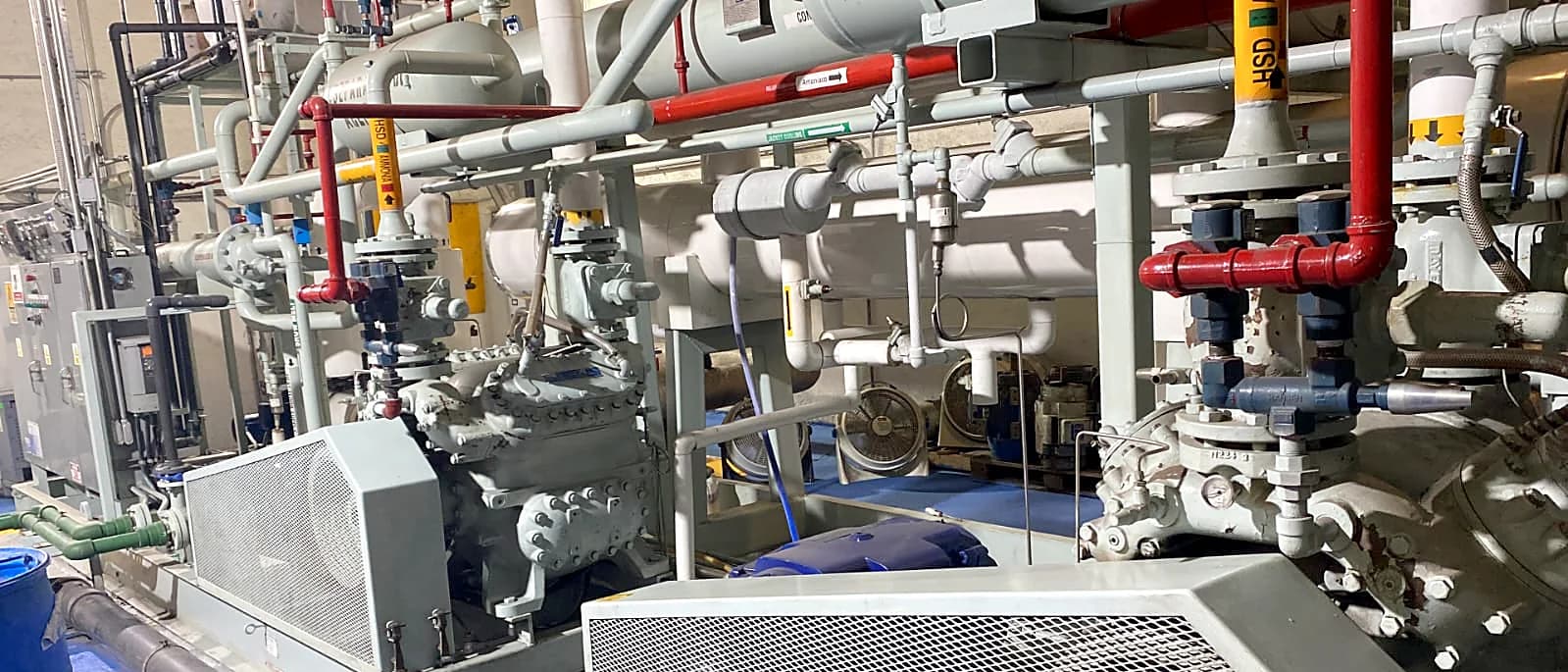 Sala de máquinas de refrigeración por amoniaco: dos compresores con sus motores, acumulador y tubería de proceso rotulada
