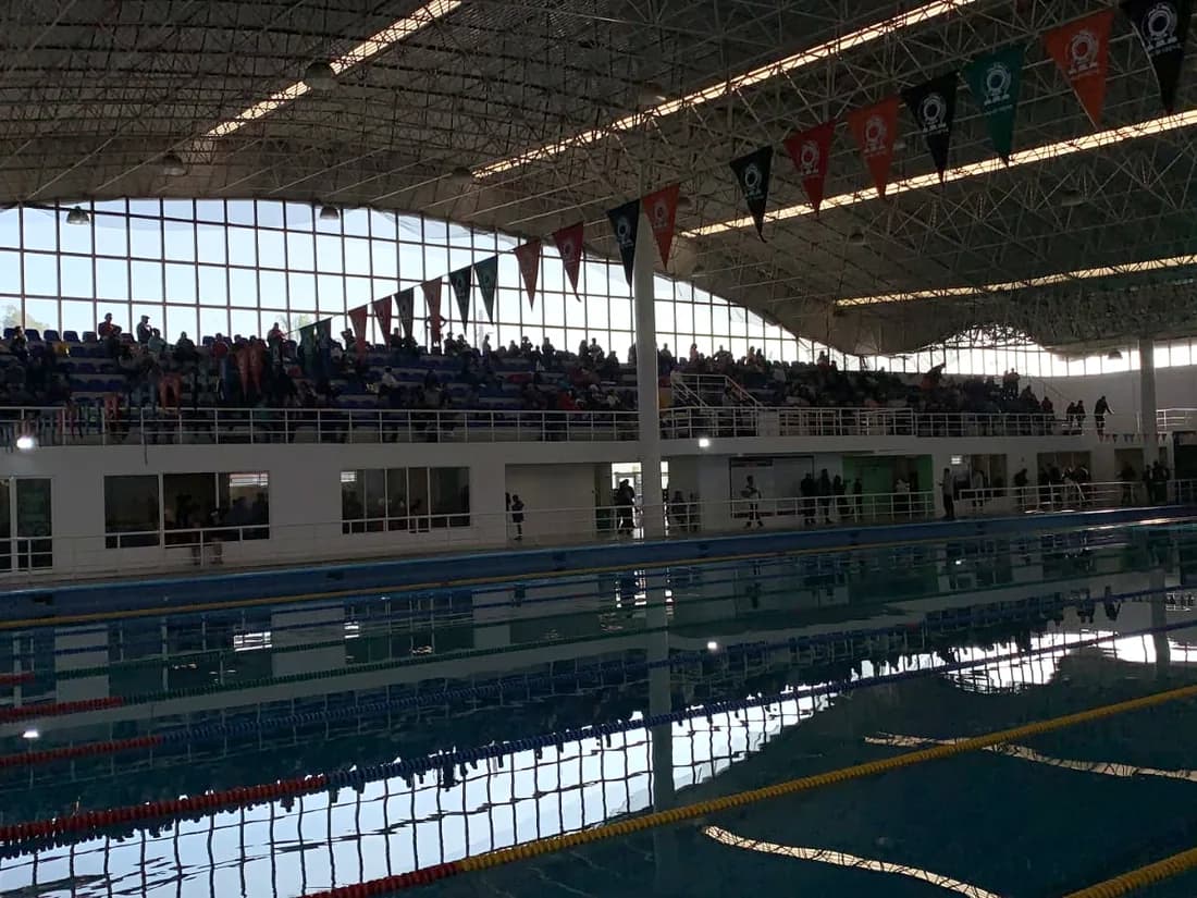 Alberca olímpica techada con gradas ocupadas durante un evento