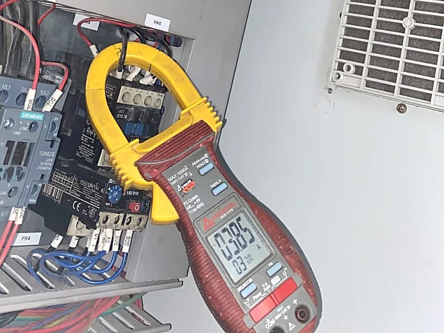 Pinza amperimétrica midiendo sobre un tablero eléctrico con contactores y protecciones